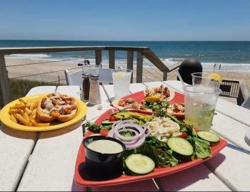 A plate of seafood salad and a shrimp po'boy sandwich with fries on an occeanside table in surf city