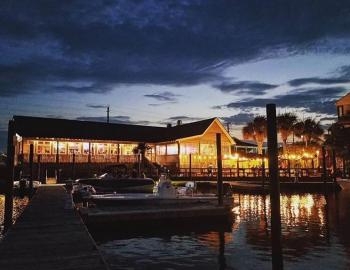 oceanside restaurant at night with a boat docked in the foreground