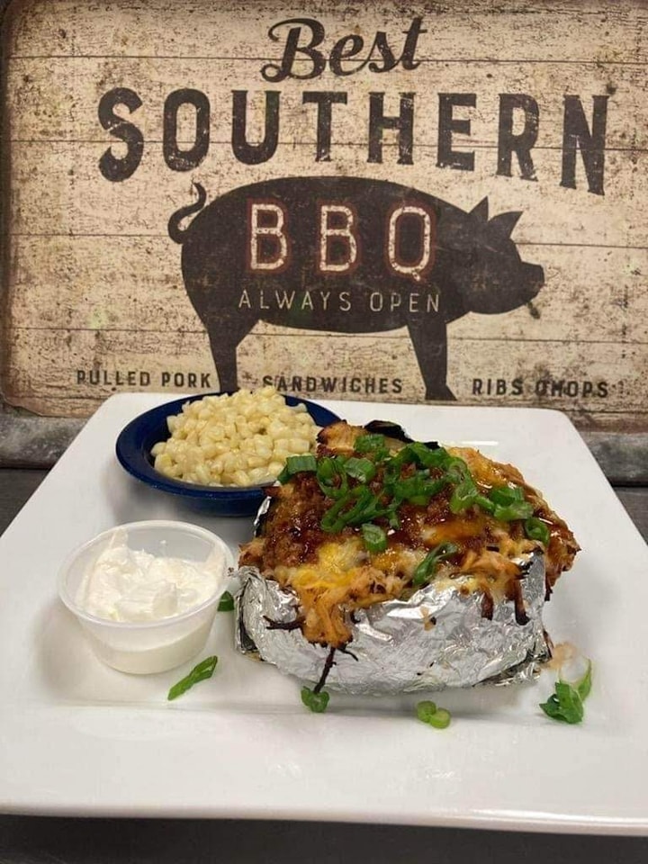 loaded barbecue baked potato and mac n' cheese on a table, in front of a sign that reads "best southern bbq"