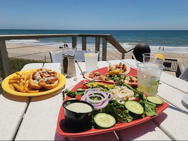 A plate of seafood salad and a shrimp po'boy sandwich with fries on an occeanside table in surf city