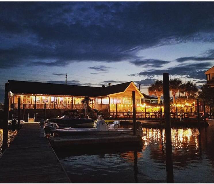 oceanside restaurant at night with a boat docked in the foreground