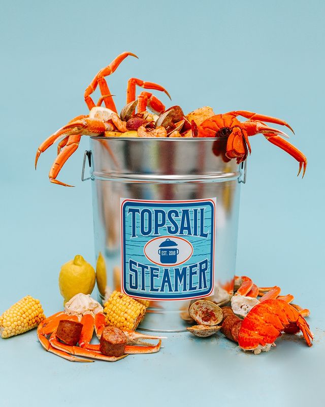 a bowl of crab legs and clams with the words "Topsail Beach" written in blue on the front